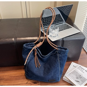 Détail du sac cabas en denim avec poignées en corde marron et pompon en cuir élégant