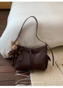 Détail d'un sac bandoulière en cuir marron foncé avec charm ours et étiquette logo sur tapis