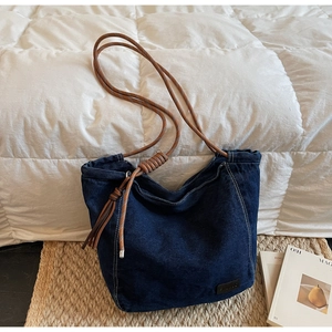Close-up of denim tote bag with brown braided rope handle and knot detail on straw mat
