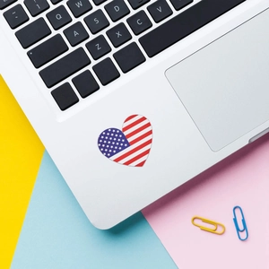 Dettaglio di un adesivo a cuore con bandiera USA su un laptop con accessori colorati