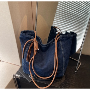 Détail du sac cabas en denim bleu avec bandoulières en corde, nœuds et glands décoratifs