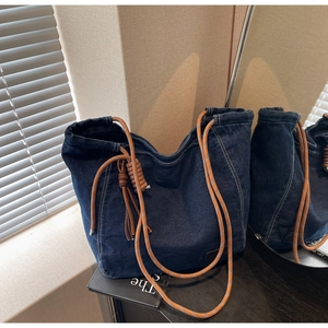 Détail du sac cabas en denim bleu foncé avec poignée en corde orange et glands en cuir
