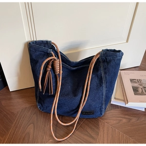 Détail d'un sac cabas en denim bleu foncé avec anses en corde tressée et pompons décoratifs