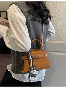 Braune Wildleder-Umhängetasche mit Goldverschluss und Hundeanhänger an einem Model
