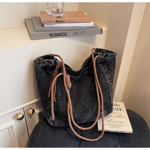 Detail of grey denim tote bag with thick rope handles and leather logo patch
