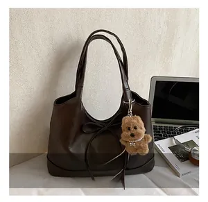 Detail of dark brown leather tote bag featuring bow drawstring and cute bear pendant charm