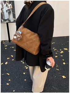 Close-up of brown quilted shoulder bag with plush bear charm in an autumn street setting