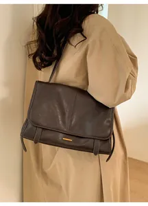 Detail der dunkelbraunen Vintage-Umhängetasche mit goldenem Akzent auf dem Trenchcoat