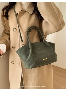 Detail of dark green tote bag with gold metal trim worn with a minimalist camel coat