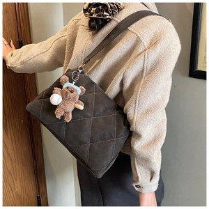 Detail of grey quilted tote bag with a small bear pendant on a dark brown leather strap