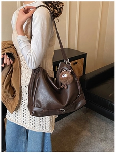 Detail of soft dark brown leather tote bag featuring a cute plush monster charm and buckle
