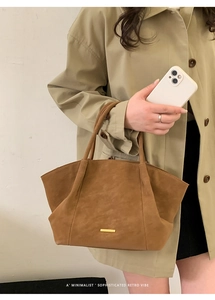 Close-up of brown suede tote bag featuring a decorative gold metal bar and stylish handle