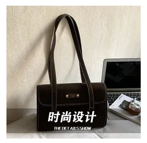 Detail of dark brown suede shoulder bag with white contrast stitching and metal plaque