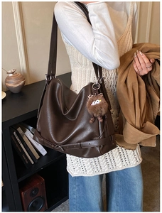 Detail of dark brown leather hobo bag with wide strap and plush monster charm pendant