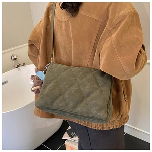 Detailed view of dark green quilted shoulder bag with cute brown bear charm accessory