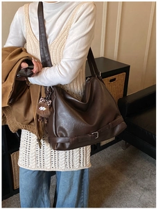 Detail of vintage brown leather tote bag with decorative buckle and plush monster charm