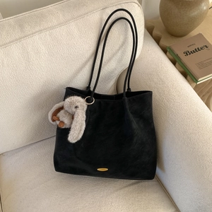 Detail of black suede tote bag on a cream sofa with a cute gray plush rabbit charm