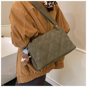 Model wearing a large olive green quilted crossbody bag with a cute bear pendant