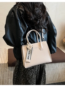 Detail of beige square handbag featuring vertical textures and a branded webbing strap
