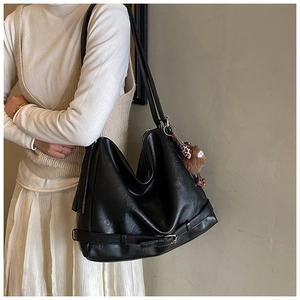 Detail of black leather hobo bag featuring belt buckle trim and brown fur pompom pendant