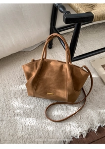 Detail of a brown matte tote bag with gold hardware on a textured rug