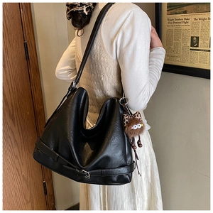 Detail of black leather hobo bag featuring a decorative buckle and plush monster charm