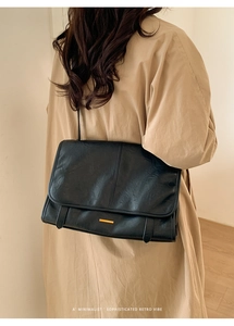 Schwarze Schultertasche aus Leder mit goldener Schnalle auf einem beigen Trenchcoat