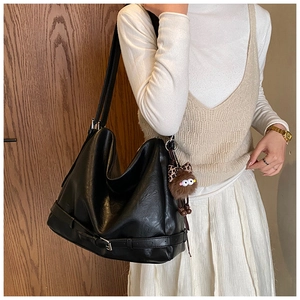 Close-up of a large black vintage shoulder bag with a decorative buckle and plush charm