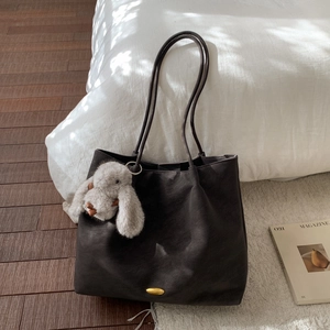 Detailed view of dark brown faux leather tote bag with plush bunny charm on wood floor
