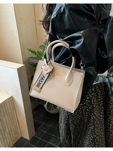 Detail of cream white textured leather crossbody bag with striped fashion ribbon