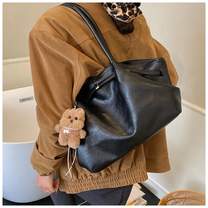Detail of black pleated tote bag with drawstring closure and cute plush bear charm