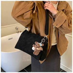 Detail of black quilted shoulder bag featuring classic rhombus patterns and plush bear charm