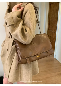 Braune Retro-Lederschultertasche mit Goldschließe an einem Model im Wollmantel