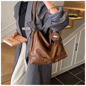 Detail of a brown leather shoulder bag featuring a fuzzy charm and strap buckle details