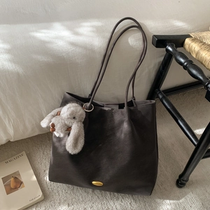 Detail of a large brown tote bag with leather texture and a plush rabbit charm