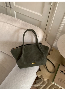 Detail of dark green suede tote bag featuring golden metal bar and long shoulder strap
