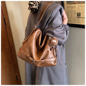 Detailed side view of brown faux leather tote bag with monster charm and metal buckle