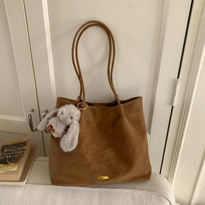 Detail of a brown suede tote bag with golden metal hardware and a plush rabbit pendant