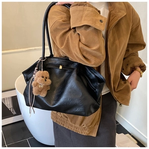 Close-up of a black slouchy leather tote bag with a cute brown plush bear charm