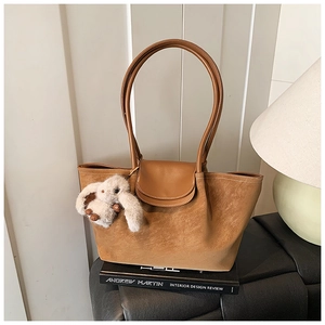 Detail of camel suede tote bag with plush rabbit charm on vintage book aesthetic