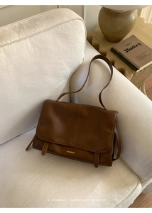 Detailansicht der braunen Retro-Ledertasche mit Goldverzierung auf weißem Sofa