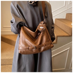 Detail of brown leather tote bag with decorative buckle strap and plush monster charm