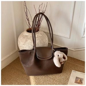 Detail of dark brown matte leather tote bag with a cute white bunny plush charm