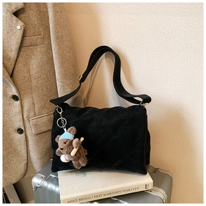 Detail of black quilted shoulder bag featuring a cute brown plush bear charm and strap