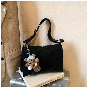 Detail of black quilted suede tote bag featuring a cute baseball bear plush keychain