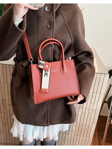 Detail of brick red striped square bag with 'BASIC' decorative strap and metal hardware