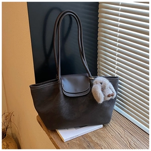 Detail of dark brown leather tote with white stitching and plush bunny charm