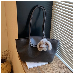 Close-up of a dark brown matte tote bag with a cute plush rabbit pendant on a wooden desk