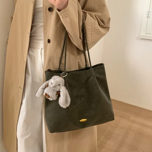 Detail of dark olive suede tote bag with golden metal hardware and a plush bunny charm
