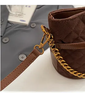 Gros plan des ferrures dorées et de la chaîne sur le sac seau en daim marron